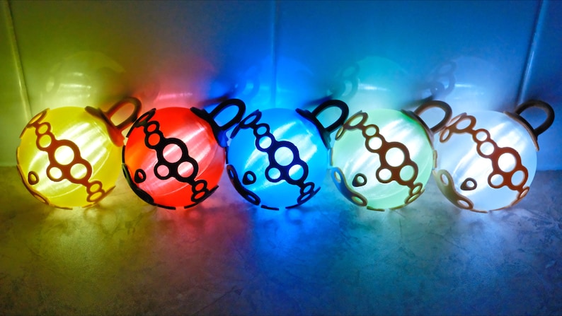May include: Five glowing, spherical decorative lights in a row, each with a unique color: yellow, red, blue, green, and white. Each sphere has a dark brown handle and a patterned design. The lights are illuminated from within, creating a vibrant display.