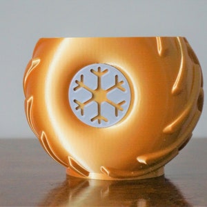 May include: A gold-colored ceramic mug with a white snowflake design. The mug has a textured exterior that resembles tire treads.