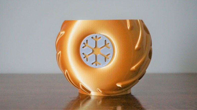 May include: A gold-colored ceramic mug with a white snowflake design. The mug has a textured exterior that resembles tire treads.