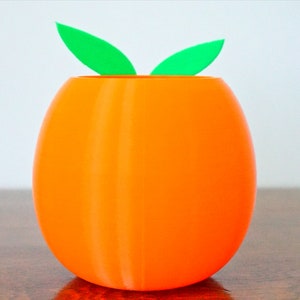 May include: Orange-colored ceramic planter shaped like an egg with two green leaves on top.