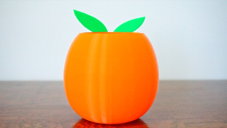 May include: Orange-colored ceramic planter shaped like an egg with two green leaves on top.