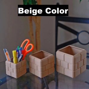 Pu&ograve; includere: Tre organizzatori da scrivania beige con motivo a mattoni, uno dei quali contiene una variet&agrave; di penne e forbici. Gli organizzatori sono su un tavolo di vetro.
