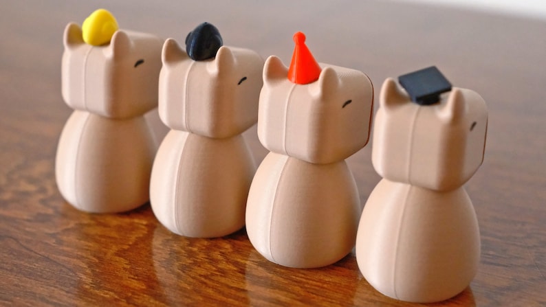 May include: Four brown ceramic figurines with different coloured hats. The hats are yellow, black, red, and black. The figurines have a simple design and are standing on a wooden surface.