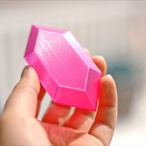 May include: A bright pink, geometrically shaped object with a smooth, slightly textured surface. The object is made of plastic and has a rounded, elongated shape.