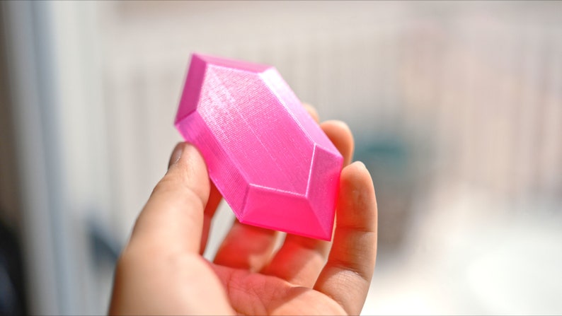May include: A bright pink, geometrically shaped object with a smooth, slightly textured surface. The object is made of plastic and has a rounded, elongated shape.