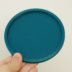May include: A teal blue round silicone coaster with a raised edge.