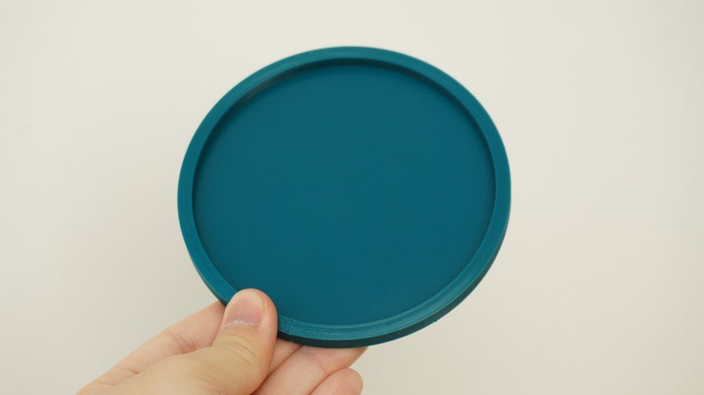 May include: A teal blue round silicone coaster with a raised edge.