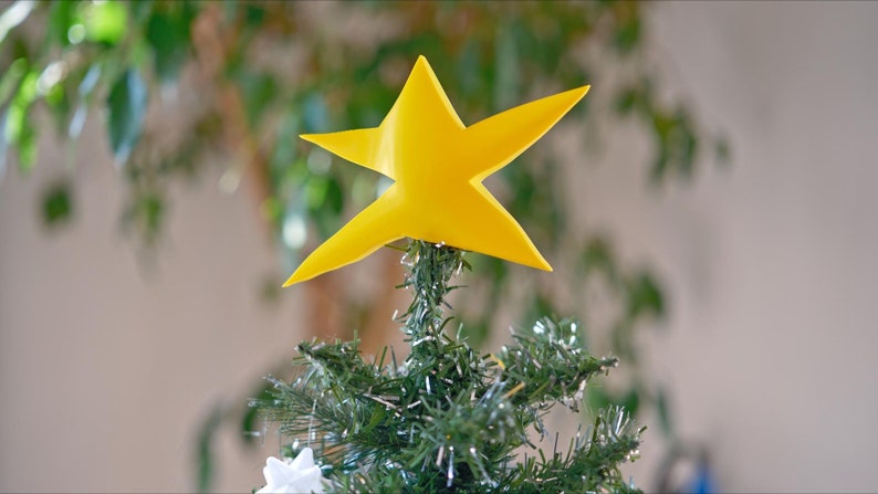 May include: A yellow paper star sits atop a green artificial Christmas tree.