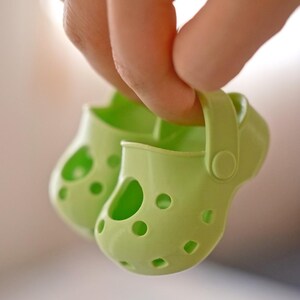 May include: A pair of light green children's shoes with holes throughout the shoe. The shoes have a strap on the back.