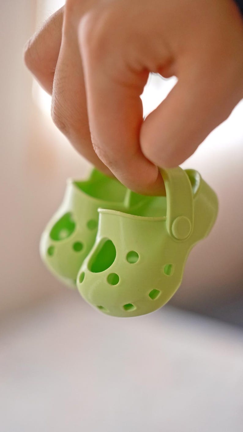 May include: A pair of light green children's shoes with holes throughout the shoe. The shoes have a strap on the back.