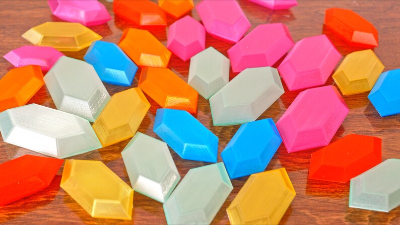 May include: A collection of colorful, geometric, faceted, plastic shapes. The shapes are in various colors, including pink, blue, green, yellow, orange, and red.