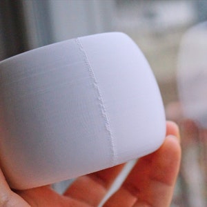 May include: A white, round, ceramic planter with a seam down the side.