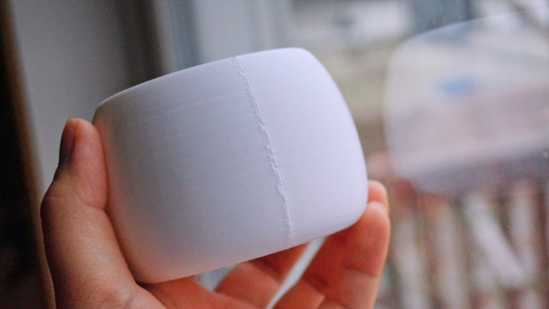 May include: A white, round, ceramic planter with a seam down the side.
