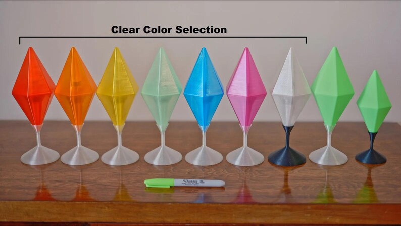 May include: A collection of nine geometric, diamond-shaped objects in various transparent colors, including orange, yellow, blue, and pink. Each object sits atop a slender stem and circular base. The phrase "Clear Color Selection" is above the objects.