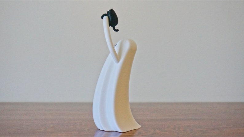 Peut inclure: Sculpture en c&eacute;ramique blanche repr&eacute;sentant une personne avec une t&ecirc;te noire et les bras lev&eacute;s au-dessus de la t&ecirc;te.