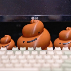 May include: Three brown ceramic figurines shaped like poop with smiling faces sitting on a white keyboard.