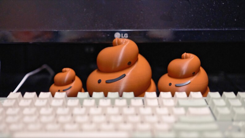 May include: Three brown ceramic figurines shaped like poop with smiling faces sitting on a white keyboard.