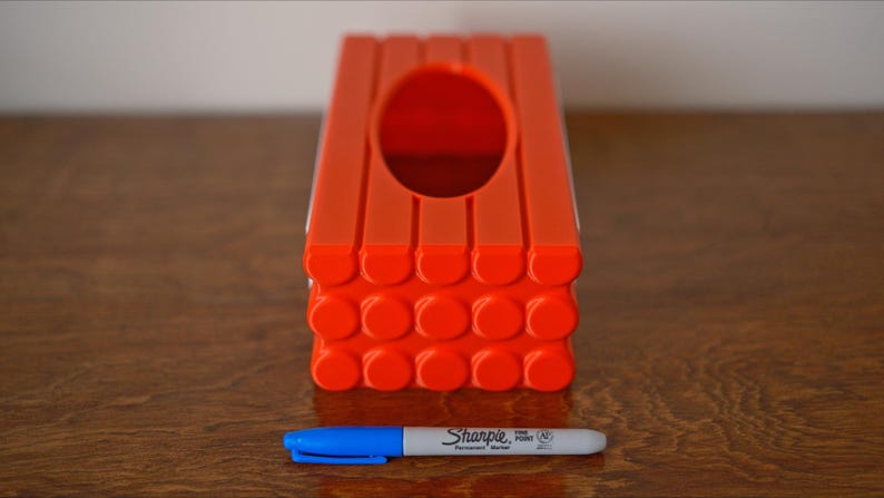 May include: Orange plastic tissue box cover with a rectangular opening and a textured bottom. The bottom is made of a series of small circles.