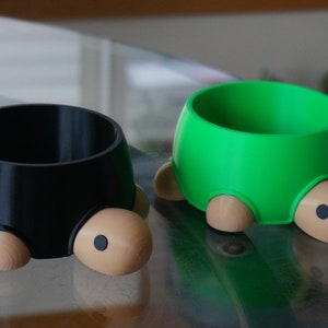 May include: Two turtle-shaped pet bowls, one black and one green, with brown legs and eyes. The bowls are made of plastic and are designed to look like turtles.
