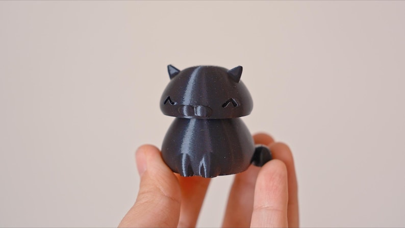 Peut inclure: Une figurine de chat noire imprim&eacute;e en 3D avec une expression mignonne. Le chat a une petite queue et est assis sur ses pattes arri&egrave;re.
