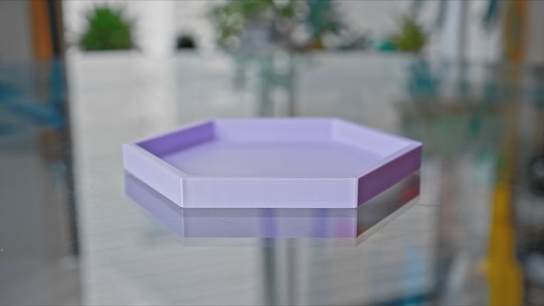 May include: A light purple hexagonal tray made of silicone. The tray is empty and sitting on a reflective surface.