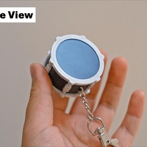 May include: A miniature drum keychain with a blue drumhead and white and black accents. The keychain includes a silver chain and clasp. The text "Underside View" is in the upper left corner.