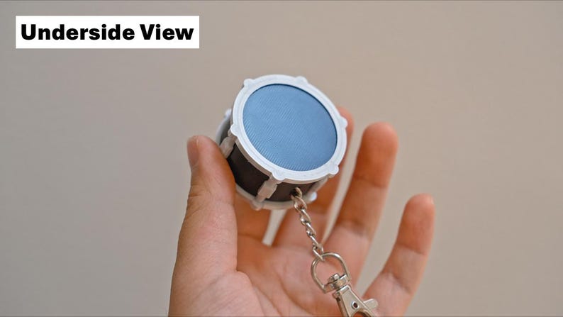 May include: A miniature drum keychain with a blue drumhead and white and black accents. The keychain includes a silver chain and clasp. The text "Underside View" is in the upper left corner.