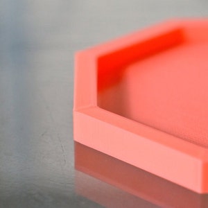 May include: A bright coral orange hexagonal tray with a smooth, slightly textured surface.