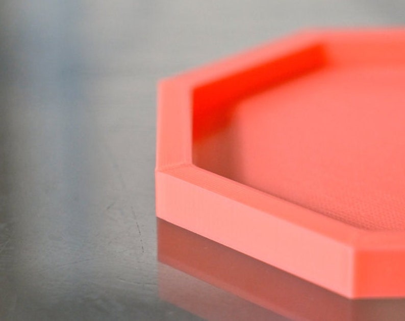 May include: A bright coral orange hexagonal tray with a smooth, slightly textured surface.