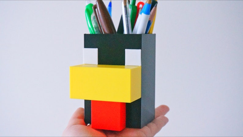 May include: A black, white, yellow, and red plastic pencil holder shaped like a Minecraft chicken.