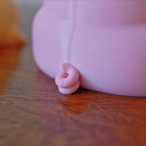 May include: A pink pig figurine with a curled tail. The pig is made of a smooth, soft material and has a rounded shape.