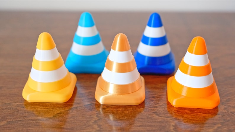 Op de afbeelding: Vijf miniatuur verkeerskegels in verschillende kleuren: blauw, goud, oranje en geel. Elke kegel heeft drie witte strepen.