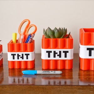 May include: Four orange Minecraft TNT-themed containers with white labels reading "TNT". The containers are different sizes and are used as planters and pencil holders.