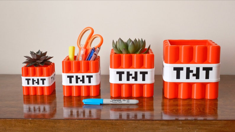 May include: Four orange Minecraft TNT-themed containers with white labels reading "TNT". The containers are different sizes and are used as planters and pencil holders.