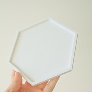 Puede incluir: Una bandeja hexagonal blanca con una superficie lisa. La bandeja est&aacute; hecha de un material duradero y es perfecta para exhibir objetos peque&ntilde;os o servir aperitivos.