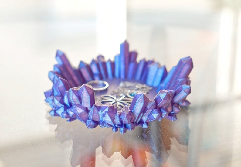 May include: A purple crystal-shaped trinket dish with an iridescent finish. The dish is filled with small jewellery items.