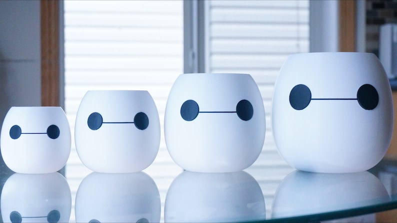 Pu&ograve; includere: Quattro vasi in ceramica bianca di diverse dimensioni, ognuno con un design in bianco e nero di Baymax, il robot del film Disney Big Hero 6.
