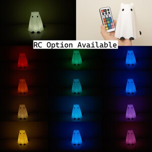 May include: A white ghost-shaped night light with a remote control. The remote control has 16 buttons for different colors, including red, green, blue, yellow, and purple. The night light is on a white surface.  RC Option Available.