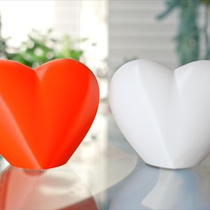 May include: Two heart-shaped ceramic ornaments, one red and one white, on a glass surface.