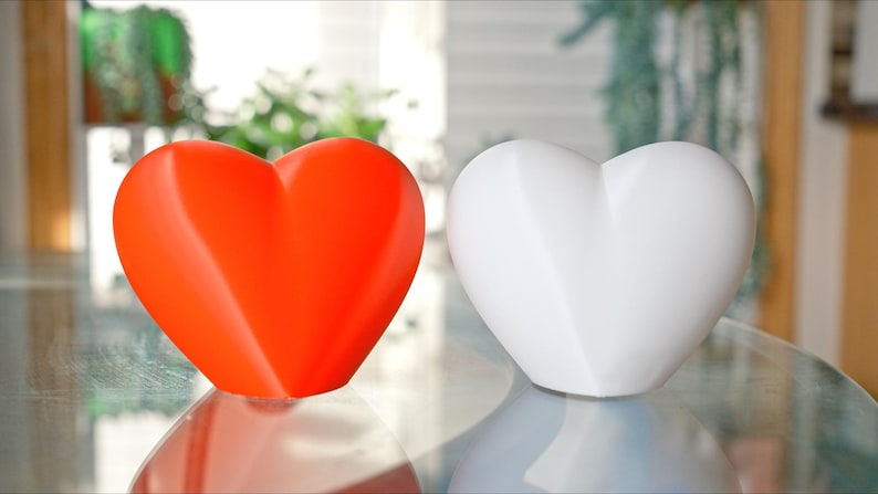 May include: Two heart-shaped ceramic ornaments, one red and one white, on a glass surface.