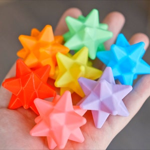 May include: A collection of seven colorful star-shaped toys, each with a different color: orange, green, blue, yellow, red, pink, and light pink.