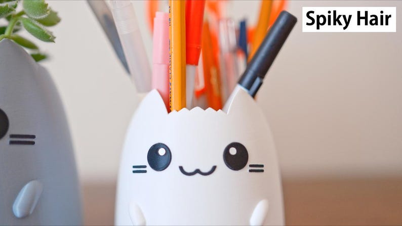 May include: A white cat-shaped desk organizer filled with pens and pencils. The organizer has a smiling face with black eyes and whiskers. The text "Spiky Hair" is in the upper right corner.