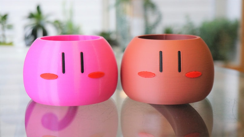 May include: Two ceramic planters shaped like Japanese dango, one pink and one brown, with black eyes and red cheeks.