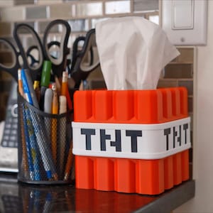 K&ouml;nnte beinhalten: Orangefarbene und wei&szlig;e Tissuebox in Form eines Minecraft TNT-Blocks. Die Box hat den Schriftzug "TNT" auf der Vorderseite.