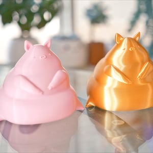 May include: Two 3D printed figurines of a chubby animal, one is pink and the other is gold.
