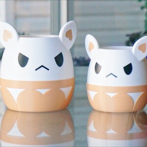 May include: Two white ceramic planters shaped like cartoon animals with angry expressions. The larger planter has brown ears and a brown bottom half. The smaller planter has white ears and a brown bottom half.