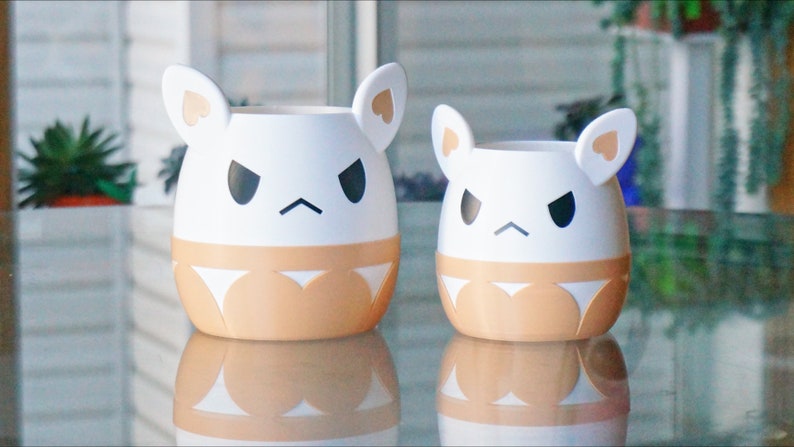 May include: Two white ceramic planters shaped like cartoon animals with angry expressions. The larger planter has brown ears and a brown bottom half. The smaller planter has white ears and a brown bottom half.