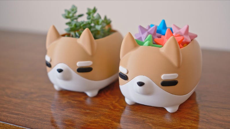 May include: Two brown ceramic planters shaped like dogs. One planter has a succulent plant inside and the other planter is filled with colorful star-shaped objects.