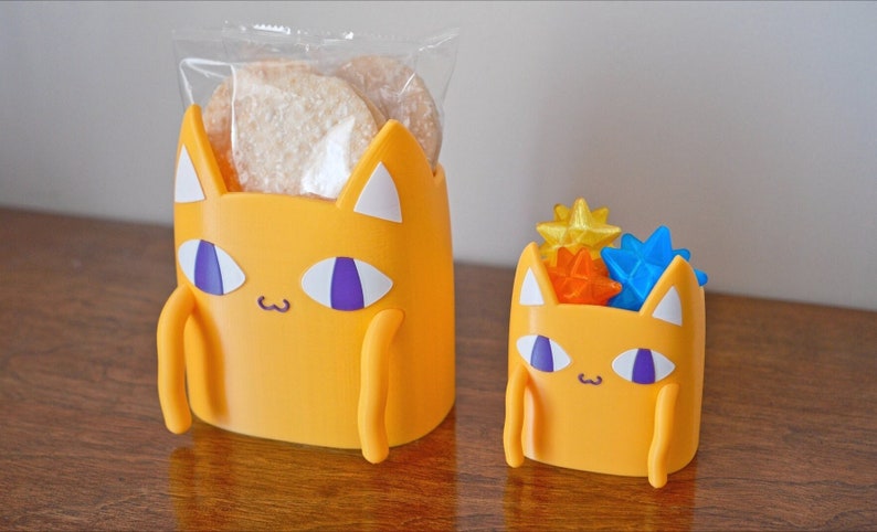 Peut inclure: Deux contenants jaunes en forme de chat. Le plus grand contient un sac en plastique transparent avec des biscuits &agrave; l'int&eacute;rieur. Le plus petit contient des objets en forme d'&eacute;toile de couleur.