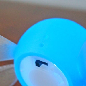 May include: A blue and white light-up fairy figurine with wings. The fairy has a small hole on the top of its head and a small black switch on the side.